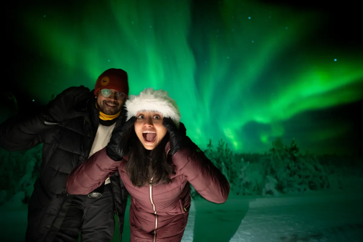 Two guests laughing under a bright green aurora