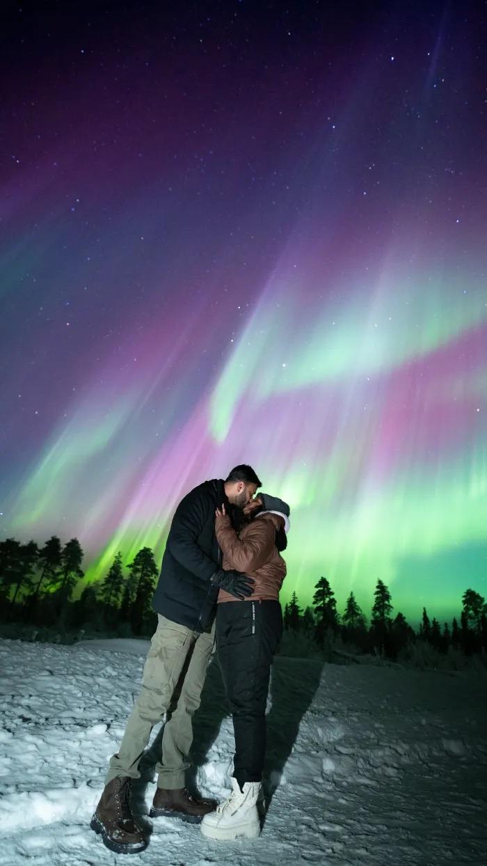 Couple beneath violet and green aurora curtains