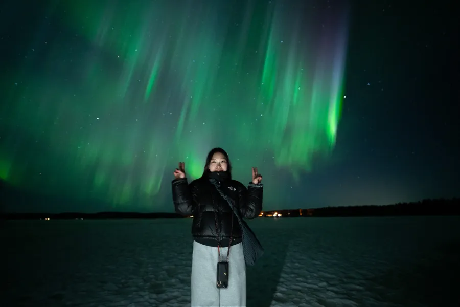 Guest with hands raised under green and violet aurora curtains