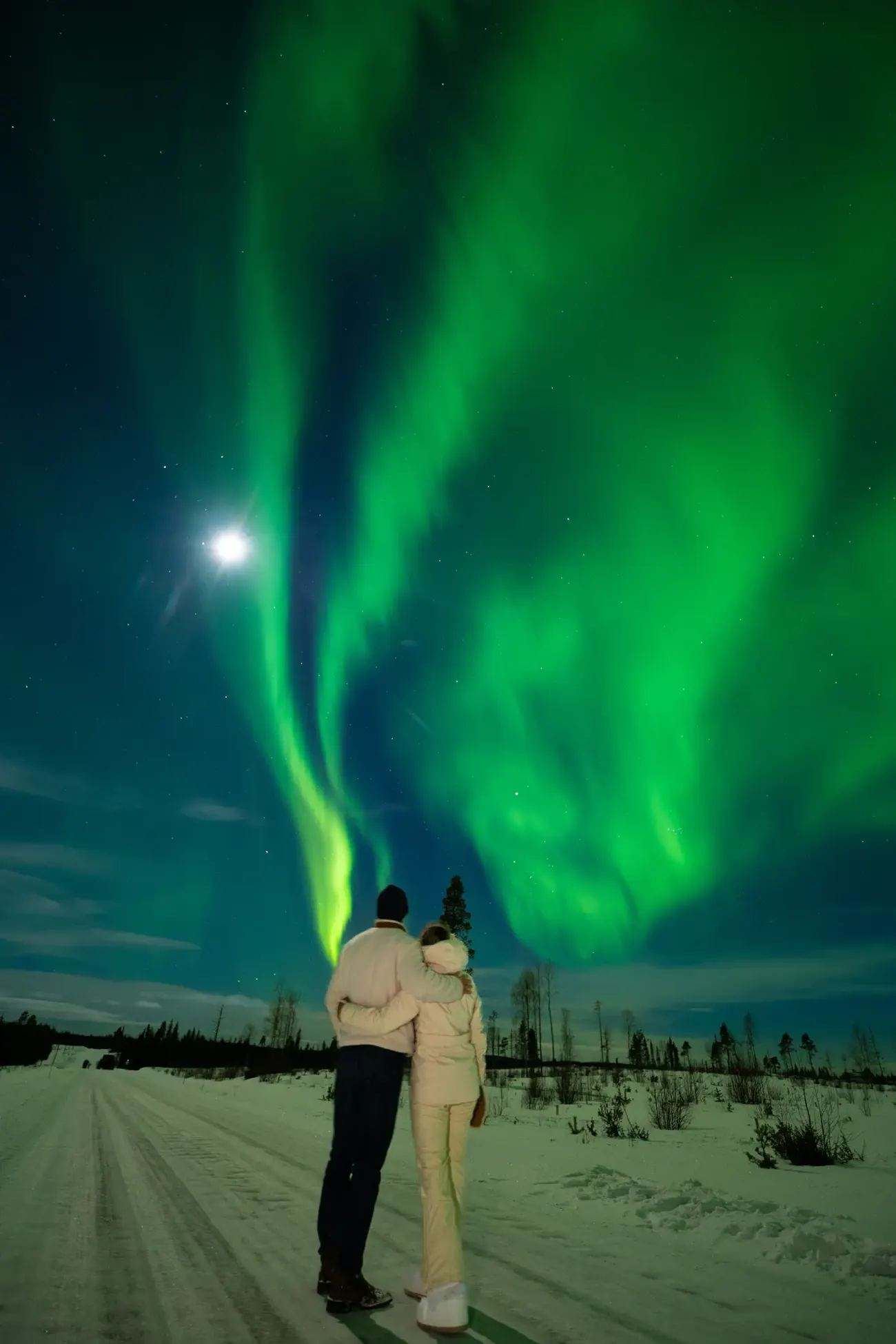 Couple under the moon and aurora on a private Arctic experience