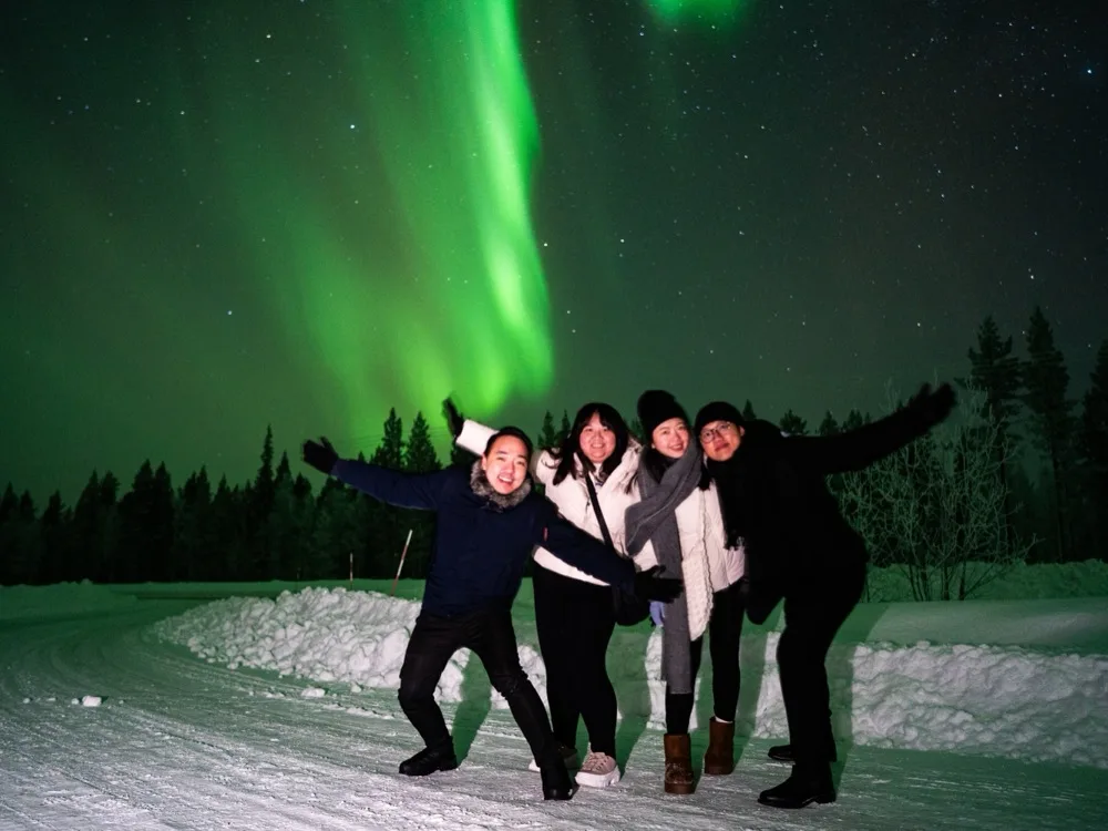 Happy group of bus tour guests posing under the Northern Lights