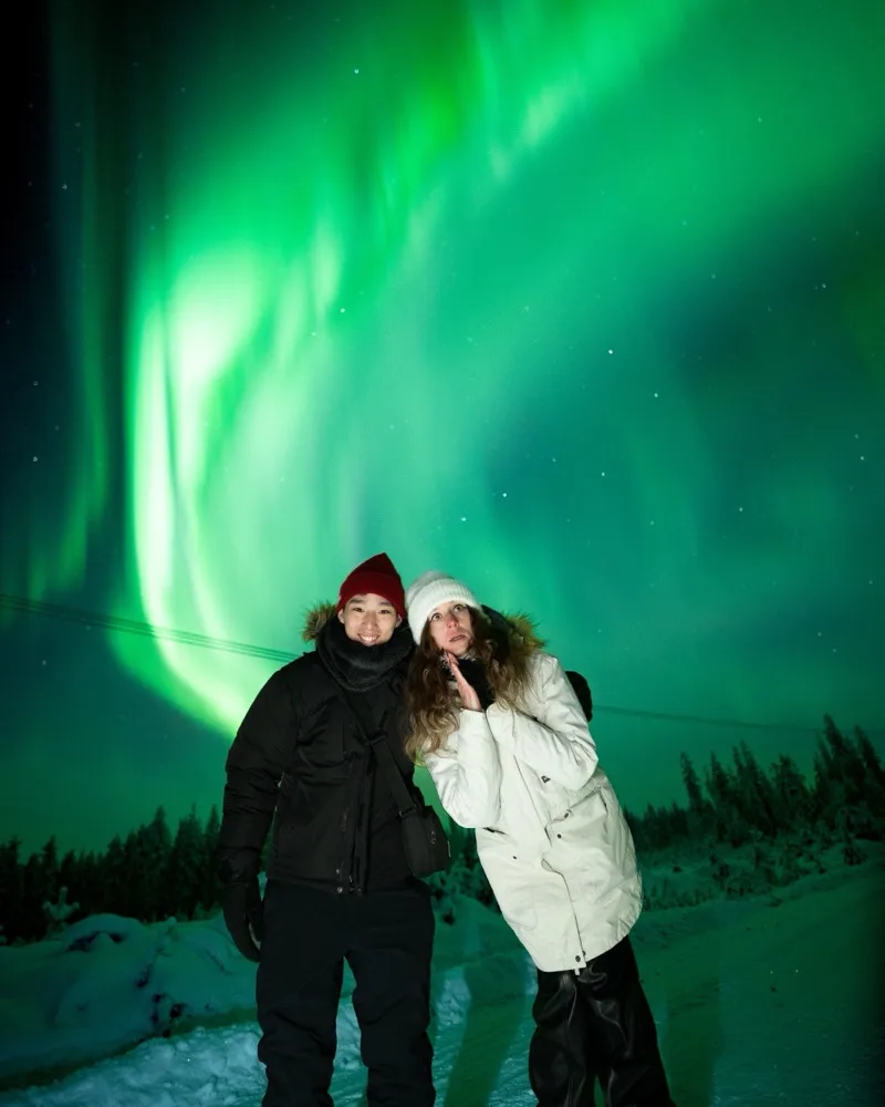Two guests marvelling at a vivid green aurora display on an Experience Tours Northern Lights hunt near Rovaniemi